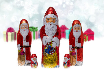 Christmas greeting card. Closeup of various cheerful wrapped chocolate Santa Claus over festive abstract blurred winter landscape. Xmas and New Year gift sweets. Macro.