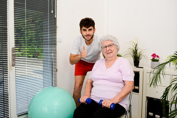 senior elderly woman with a personal trainer private fitness coach at home handsome young man