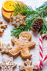 Christmas gingerbread and sweets are placed on wooden desk. Cookies and sweet food in shape of stars and snow flakes. Winter theme, rustic style. Pine trees on the side. Candy stick and other spice.