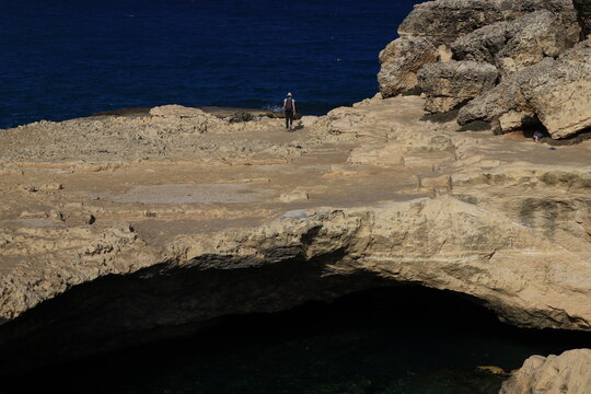 A walker strolls on the overhang above the grotta della poesia (Puglia, Italy)