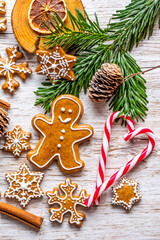 Christmas gingerbread and sweets are placed on wooden desk. Cookies and sweet food in shape of stars and snow flakes. Winter theme, rustic style. Pine trees on the side. Candy stick and other spice.