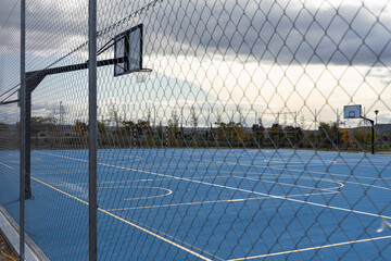 blue colored outdoor basketball court behind a fence