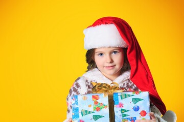 Portrait of a satisfied little child in Christmas Santa hat. Holds a gift box. Preparing for the New Year holidays