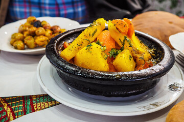 Tajine or tagine - traditional Berber dish served in black earthenware bowl at typical Moroccan street restaurant, closeup detail