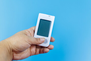 Digital glucometer in female hand over a pastel blue background. Diabetes concept