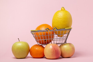 Fruits in a small shopping basket on a pink background. Buy fruit. Supermarket shopping concept.