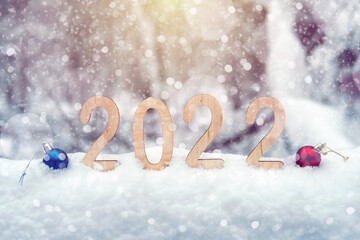 Fototapeta na wymiar 2022 plywood new year numbers in a snowdrift outdoors in winter forest with Christmas balls, snowflakes and sun rays. Shallow depth of field. Happy new 2022 year