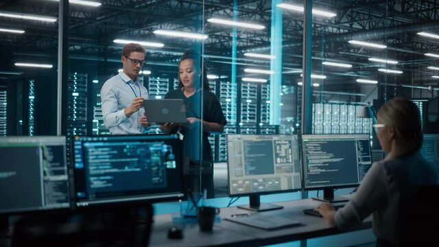 Big Data Center Server Room: Female e-Business Enrepreneur and Male IT Specialist talk, Use Laptop. Information Technology Engineer and System Administrator work on Web Services Cloud Computing SAAS