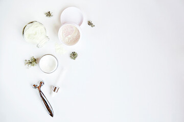 Face care cosmetics set on white background with copy space. Dermatology cosmetics. Face cream, alginate mask and massager. Natural eco forest moss decoration.
