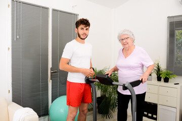 senior elderly woman with a personal trainer private fitness coach at home handsome young man