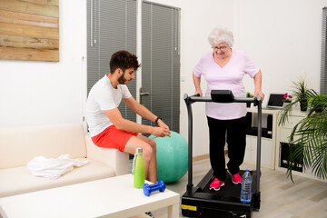 senior elderly woman with a personal trainer private fitness coach at home handsome young man