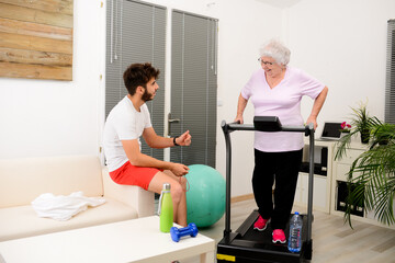 senior elderly woman with a personal trainer private fitness coach at home handsome young man