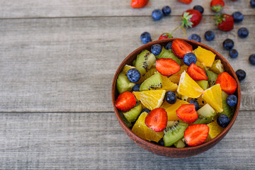 Healthy fresh fruit salad in brown bowl on gray background. Top view