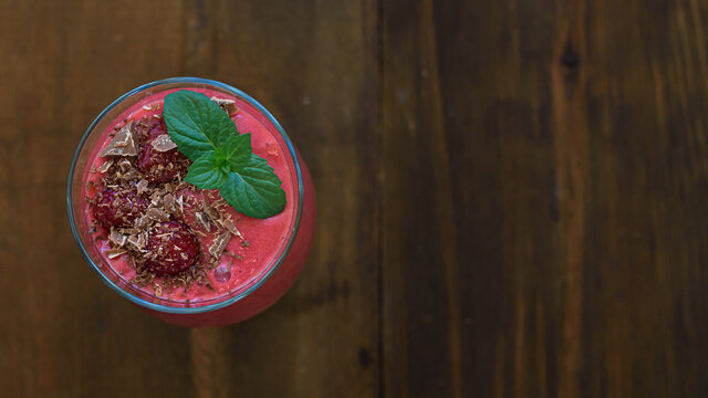 Raspberry smoothie in glass on wooden table.Top view. Smoothie sprinkled with grated chocolate