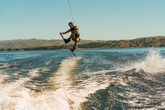 young man doing wakeboarding in a lake whit mountains also doing jumps