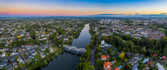 Aerial drone panoramic view at sunset, looking up the Waikato River towards the CBD, over the city of Hamilton (Kirikiriroa) in the Waikato region of New Zealand. - obrazy, fototapety, plakaty