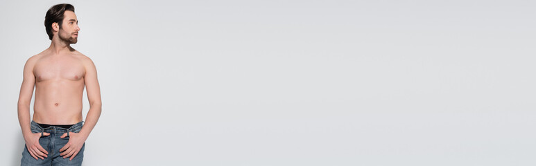 Fototapeta premium sexy shirtless man in jeans looking away while posing with thumbs in belt loops on grey, banner.