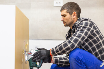 A carpenter with a corded jigsaw cutting a part of the wooden surface (board)