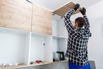 The carpenter sets the door of the kitchen shelves