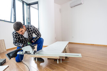 A carpenter cutting a wooden board on the floor of the room
