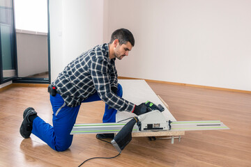 A carpenter cutting a wooden board on the floor of the room