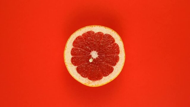 TOP VIEW: Half of an grapefruit rotates on a red surface - Slow motion