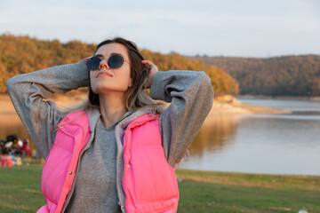 A beautiful girl with sun glasses standing in front of the lake. Girl in pink coat. Beauty and fashion concept.