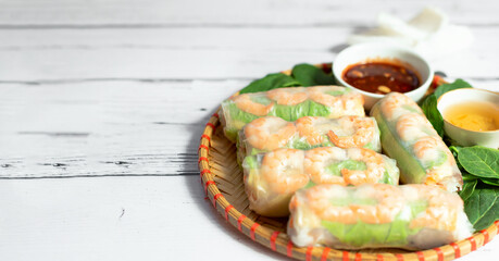 Vietnamese spring rolls with tender chicken, tiger prawns, rice noodles, juicy mango, fresh herbs on a wooden board. Sesame sauce. Traditional Vietnamese healthy food