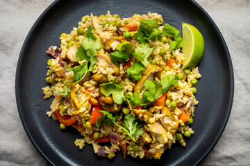 Chicken curry with green peas, red pepper, coriander, lime and basmati rice, served in a dark plate.