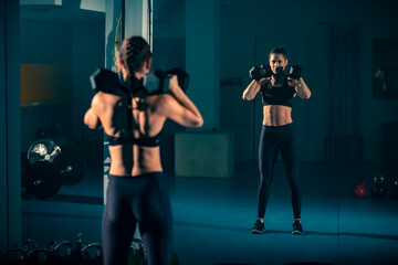 A young female doing exercise with a two dumbbell in front of a mirror