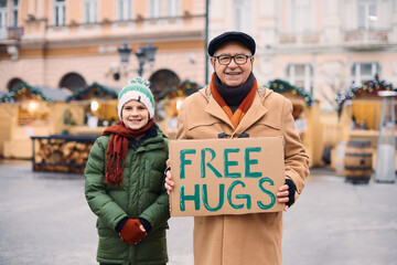 Happy grandfather and grandson offering free hugs at Christmas market during winter holidays.