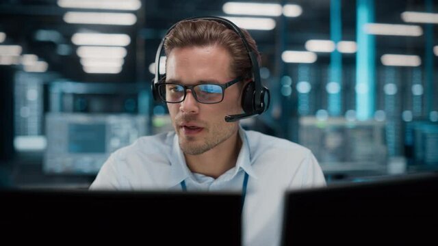 Call Center Office: Portrait of Friendly Caucasian Male Technical Customer Support Specialist Talking on a Headset, uses Computer. Client Experience Officer Helps Online via Video Conference
