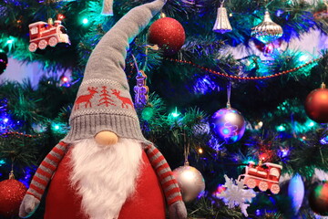 Świąteczny skrzat, krasnal na tle choinki. A Christmas gnome, a leprechaun with a Christmas tree background. - obrazy, fototapety, plakaty