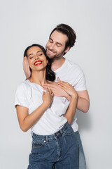 smiling man embracing happy brunette woman standing with closed eyes on grey.