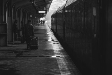 Black and white and (film noir, atmospheric) image with a man carrying a luggage near a train ready to leave from a train station on a snowy cold winter day.