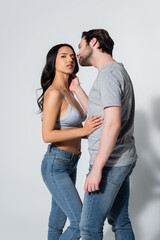 man in t-shirt seducing woman in jeans and bra on grey.