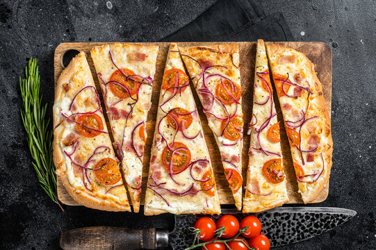 Homemade Flammkuchen or tarte flambee with cream cheese, bacon, tomato and onions. Black background. Top view