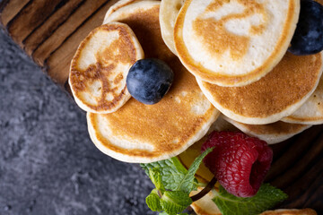 Stack of pancakes with berries on wooden board. Dark wooden background