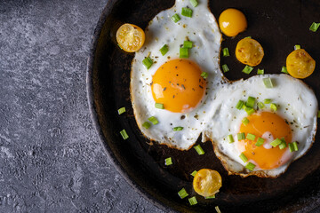 breakfast with fried eggs in a pan with bacon and vegetables on dark background