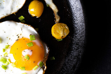 breakfast with fried eggs in a pan with bacon and vegetables on dark background