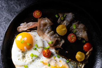 breakfast with fried eggs in a pan with bacon and vegetables on dark background