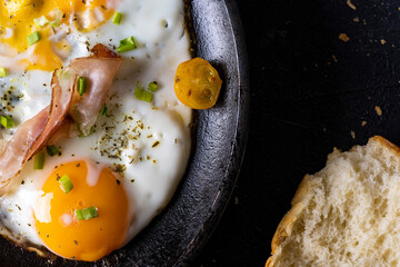 breakfast with fried eggs in a pan with bacon and vegetables on dark background