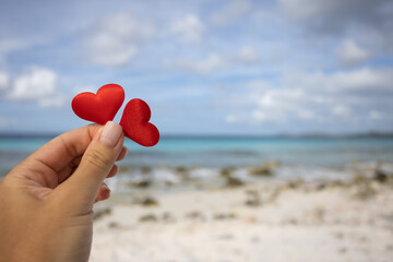 Fototapeta premium Female hand holding two small hearts on the background of the seascape.