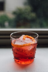 electric red orange Negroni cocktail on window sill with lush green background