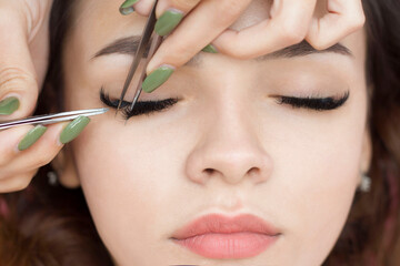 Eyelash extensions. a young woman undergoes a close-up eyelash extension procedure. Tweezers.