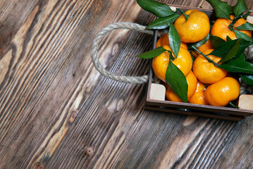 Fresh tangerines with green leaves in an old box. On wooden background.