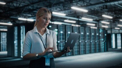 Successful Female Chief Technology Officer Using Laptop Computer, Standing in Big Warehouse Data Center. System Administrator Maintenance of SAAS, Cloud Services Server. Digital Entrepreneur. Static - Powered by Adobe