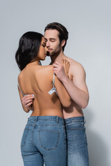 shirtless man with closed eyes taking bra off sexy woman in jeans on grey.