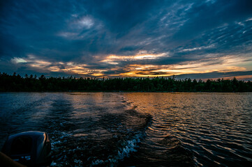 Landscape of a lake surrounded by trees under a stormy cloudy sky in the evening
