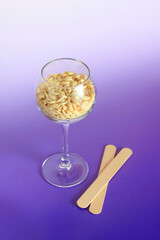 hot depilation wax granules in glass and wooden spatulas on violet background. beauty industry, body care